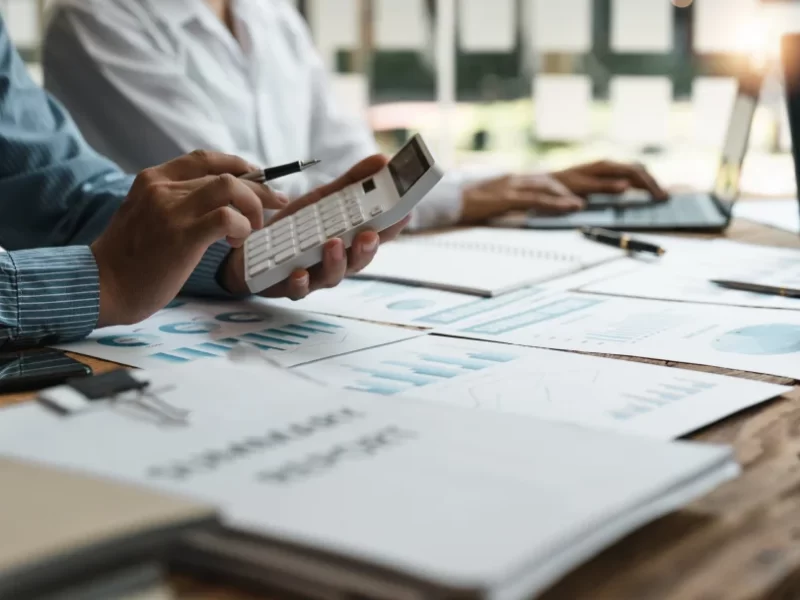 Des professionnels collaborent sur un ordinateur portable et des documents, illustrant un environnement de travail dynamique.