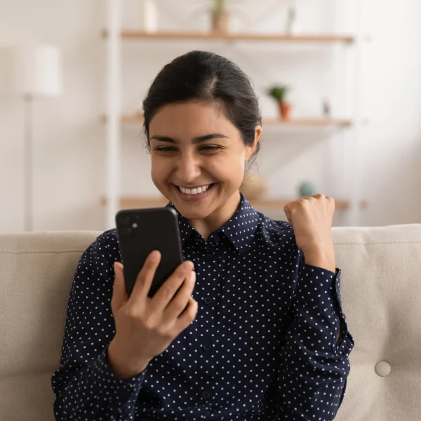 A woman smiles while using her phone, representing ease and accessibility in obtaining a loan without a credit check.