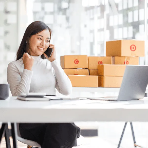 A woman sitting at a desk, working on a laptop surrounded by boxes