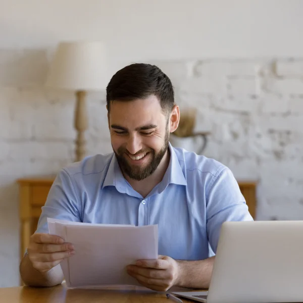 A man smiles while reviewing a paper, likely containing his credit score, reflecting satisfaction and optimism.