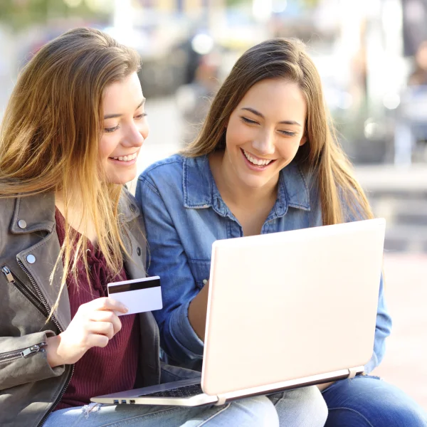 Two young women seated on the ground, focused on a laptop, discussing financial options related to a line of credit.