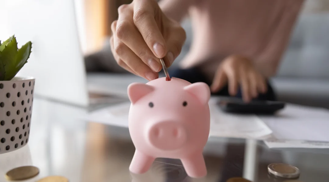 A woman deposits coins into a piggy bank, symbolizing savings and financial management through refinancing.