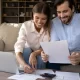A couple sits on a couch, reviewing paperwork related to their online loan application.