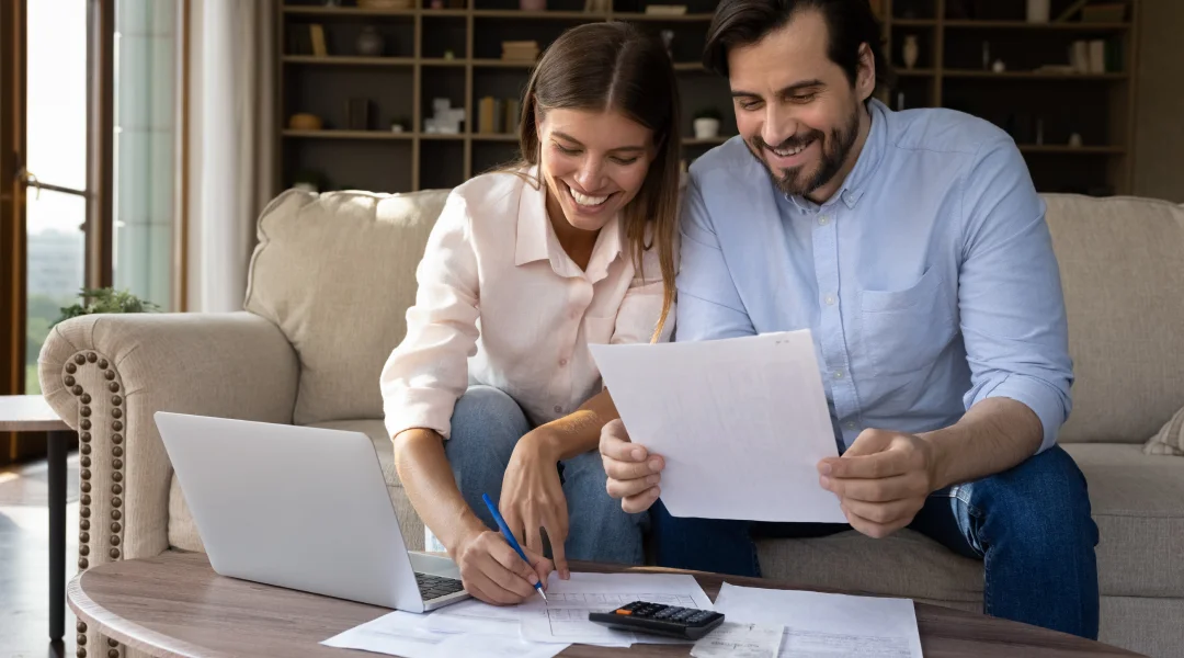 A couple sits on a couch, reviewing paperwork related to their online loan application.