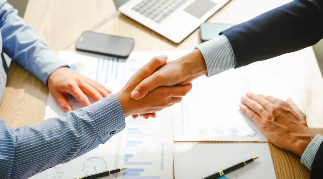 Deux professionnels se serrent la main au-dessus d'une table, symbolisant un accord commercial lié à la cote de crédit.